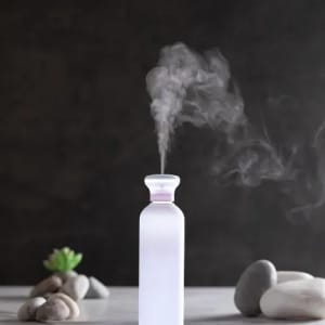 A drink bottle in frosted white with purple detailing, emitting a gentle mist against a dark background.