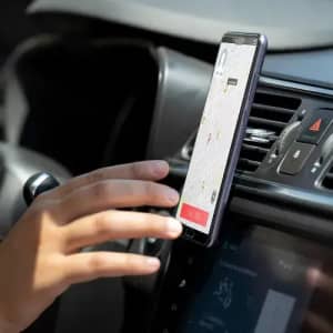 A smartphone mounted in a car, displaying a map, with a hand reaching towards the screen. The dashboard has a modern design.