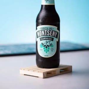 A drink bottle with a black body and aqua label, placed on a small wooden pallet. It has a logo and branding details.