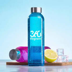 A drink bottle in blue with a logo, placed next to a pink bottle, lime, and ice cubes on a wooden tray.