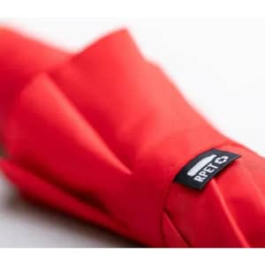 A red umbrella featuring a black branding label on the shaft, neatly folded and resting on a surface.