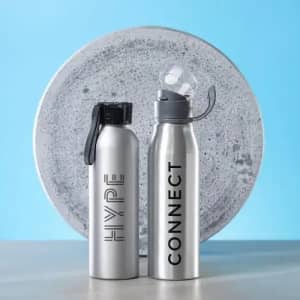 Two stainless steel drink bottles with different caps, placed beside a round concrete item against a blue background.