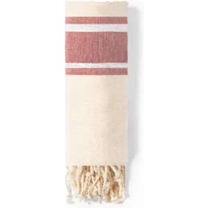 A woven towel in cream with red stripes and tassels at one end. It features a simple, textured design.