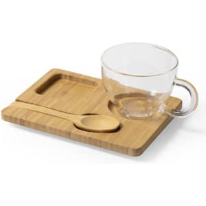 A glass cup with a handle sits on a bamboo tray, accompanied by a wooden spoon.