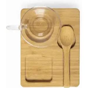 A wooden serving tray with a clear glass cup, a wooden spoon, and a small square dish.
