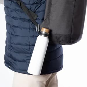 A drink bottle with a white body and a cork lid is attached to a black bag on a person's side.