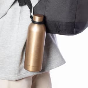 A drink bottle in a metallic gold finish, hanging from a bag strap with a black holder.