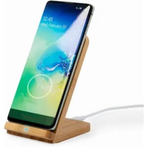A phone stand featuring a bamboo base, holding a smartphone with a green charging indicator on the screen.