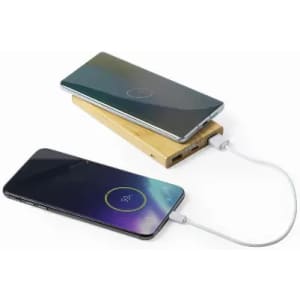 A wireless charger in a wooden base with two smartphones, one charging and one in use, connected by a cable.