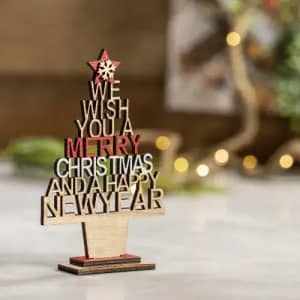 A decorative wooden sign with festive text, featuring red and natural wood hues, arranged in a Christmas tree shape.