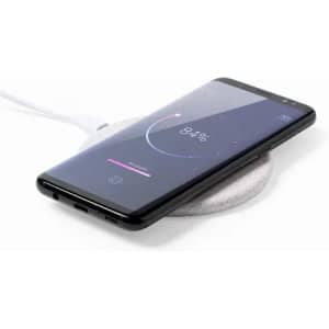 A phone is placed on a round, grey wireless charging pad with a white cable connected. The screen displays a battery percentage.