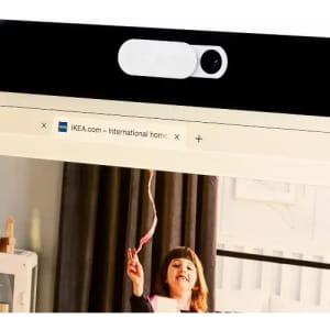 A webcam with a white cover located on a computer monitor displaying a web page. The setting includes a child playing.