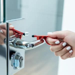 A red door opener tool is being used to pull open a chrome door handle. The setting is modern and sleek.