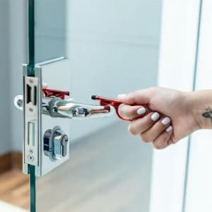 A hand using a red door handle tool to open a glass door, showcasing a sleek, modern design.