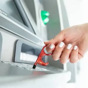 A red ATM tool being used to press buttons on an ATM, with a hand featuring white nail polish in focus.
