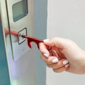 A red hygiene key is being used to press a button on an elevator panel. The key features a hook design.