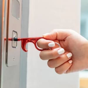 A red door opener tool is being used to press a button. The hand has manicured white nails.