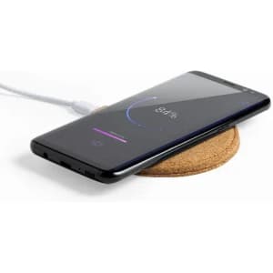 A smartphone charging on a round cork wireless charger, with a charging indicator showing 84%.