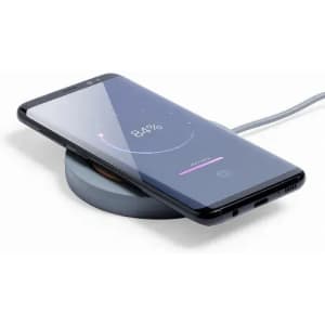 A wireless charging pad with a smartphone placed on it, featuring a sleek black design and a grey base.