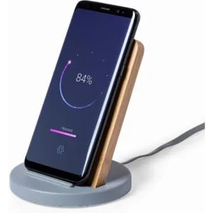A wireless charging stand with a grey base and a wooden back, holding a smartphone displaying a charging status.