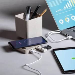 A desk setup featuring a beige storage pot with pens, a smartphone charging on a pad, and a laptop with graphs.