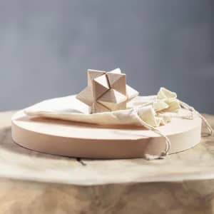 A wooden puzzle with geometric shapes rests on a circular wooden base next to a small cloth bag.