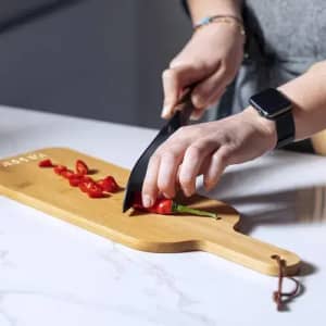 A wooden chopping board with a black knife, featuring sliced red chillies, on a marble surface.