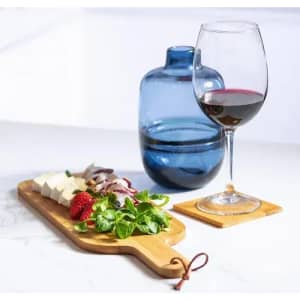 A drink bottle in blue beside a glass of red wine and a wooden platter of cheese, strawberries, and greens.