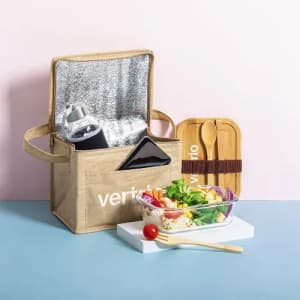 A lunch bag in beige with a drink bottle, utensils, and a bowl of salad beside it on a pastel background.