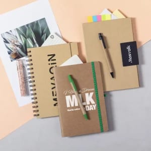 A collection of notebooks and stationery items in neutral tones, featuring a green pen and sticky notes.