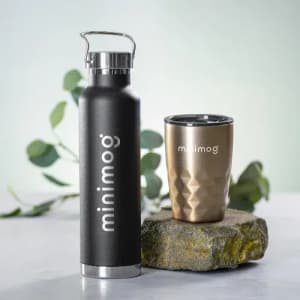 A drink bottle and a cup in black and bronze, featuring a logo on each. Both are displayed on a stone surface.