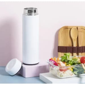 A drink bottle in white with a silver lid, placed next to a salad and wooden utensils on a pink background.