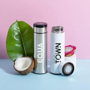 A drink bottle in silver and white with a logo, surrounded by a coconut, dragon fruit, and a green leaf.