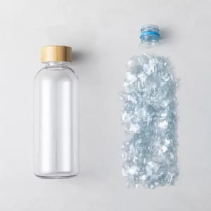 A drink bottle made of clear glass with a bamboo lid, alongside a bottle filled with blue plastic fragments.