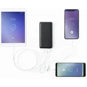 A power bank in black connected to two smartphones and a tablet, all displaying battery status indicators.