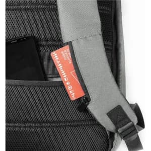 A grey backpack featuring a black mesh pocket with a phone and a red tag partially visible. It has an adjustable strap.