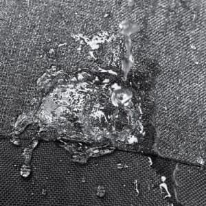 A close-up of water droplets splashing on a textured dark fabric surface, highlighting its water-resistant properties.