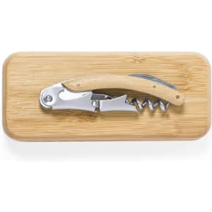 A corkscrew with a wooden handle lies on a bamboo cutting board. The corkscrew has a silver finish.