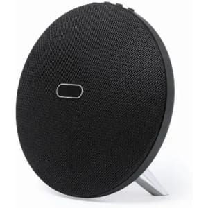 A round black speaker with a textured surface and a stand on the back. It features a simple logo.