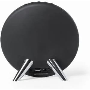 A round black speaker with silver legs, featuring ports on the back for connectivity.