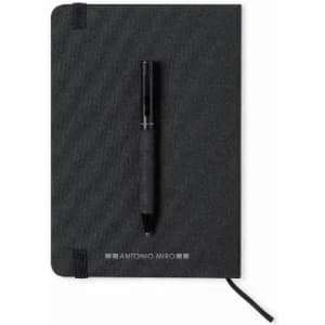 A black notebook with a pen resting on top, featuring a logo on the front cover.