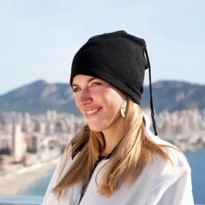 A woman wearing a black beanie hat, smiling against a scenic mountainous backdrop and city skyline.