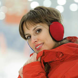 A woman in a red jacket and red earmuffs smiles, with a blurred background of soft lights.