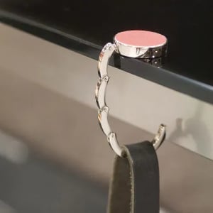 A metallic hook with a red top, designed to hang items, attached to a black surface.