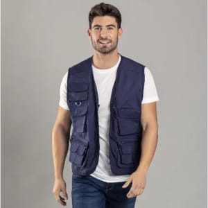 A man wearing a navy blue multi-pocket vest over a white t-shirt, standing against a grey background.