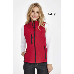 A red women's softshell vest with a zip front and pockets, worn over a white long-sleeve top. It features a logo.
