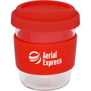 A reusable coffee cup with a transparent body, red silicone lid, and a red silicone band. It features a logo.