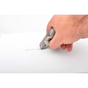 A correction tape dispenser in grey, being used to cover handwritten text on white paper.
