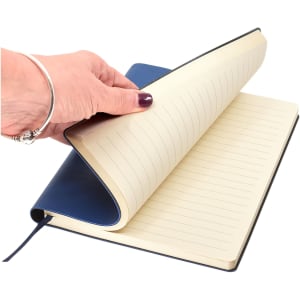 A hand holding a blue A5 notebook with lined pages, featuring a smooth cover and a ribbon bookmark.
