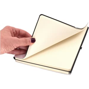 A hand holding an open A5 notebook with blank pages, featuring a black and white cover.
